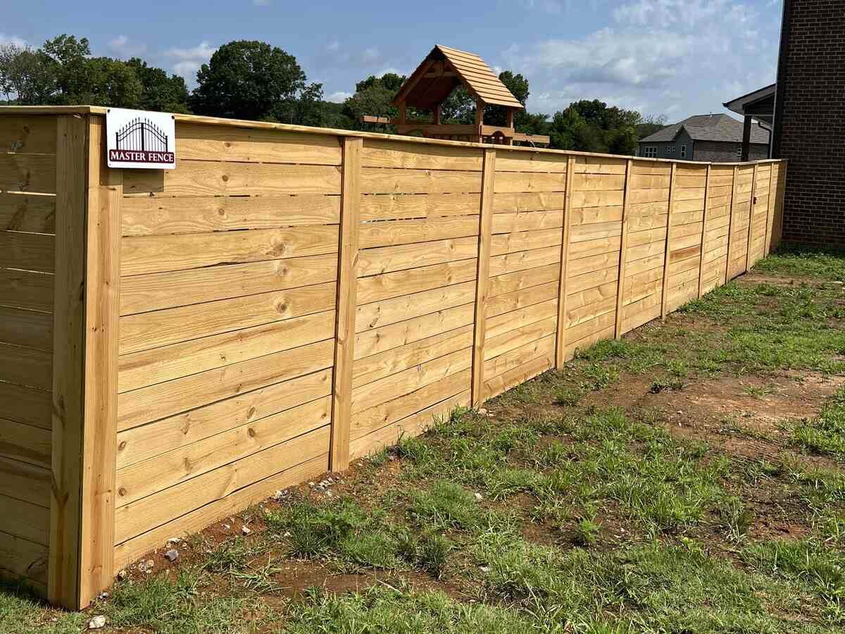 Horizontal wood privacy fence with a tabletop design installed around a backyard with a playground